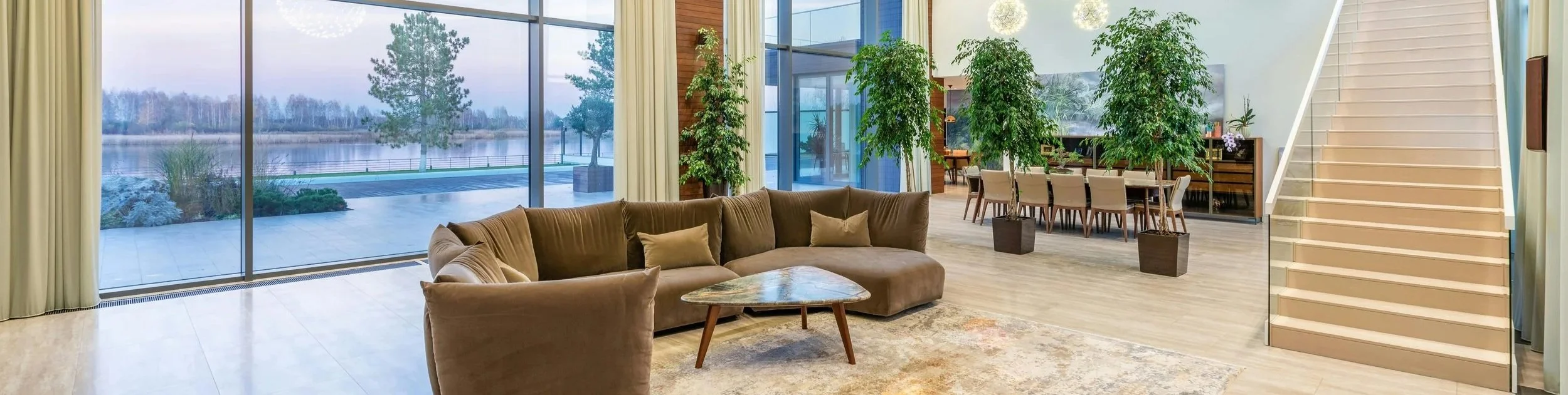 Modern condo building entryway interior featuring a caramel-colored velvet couch against large glass windows looking outdoors.