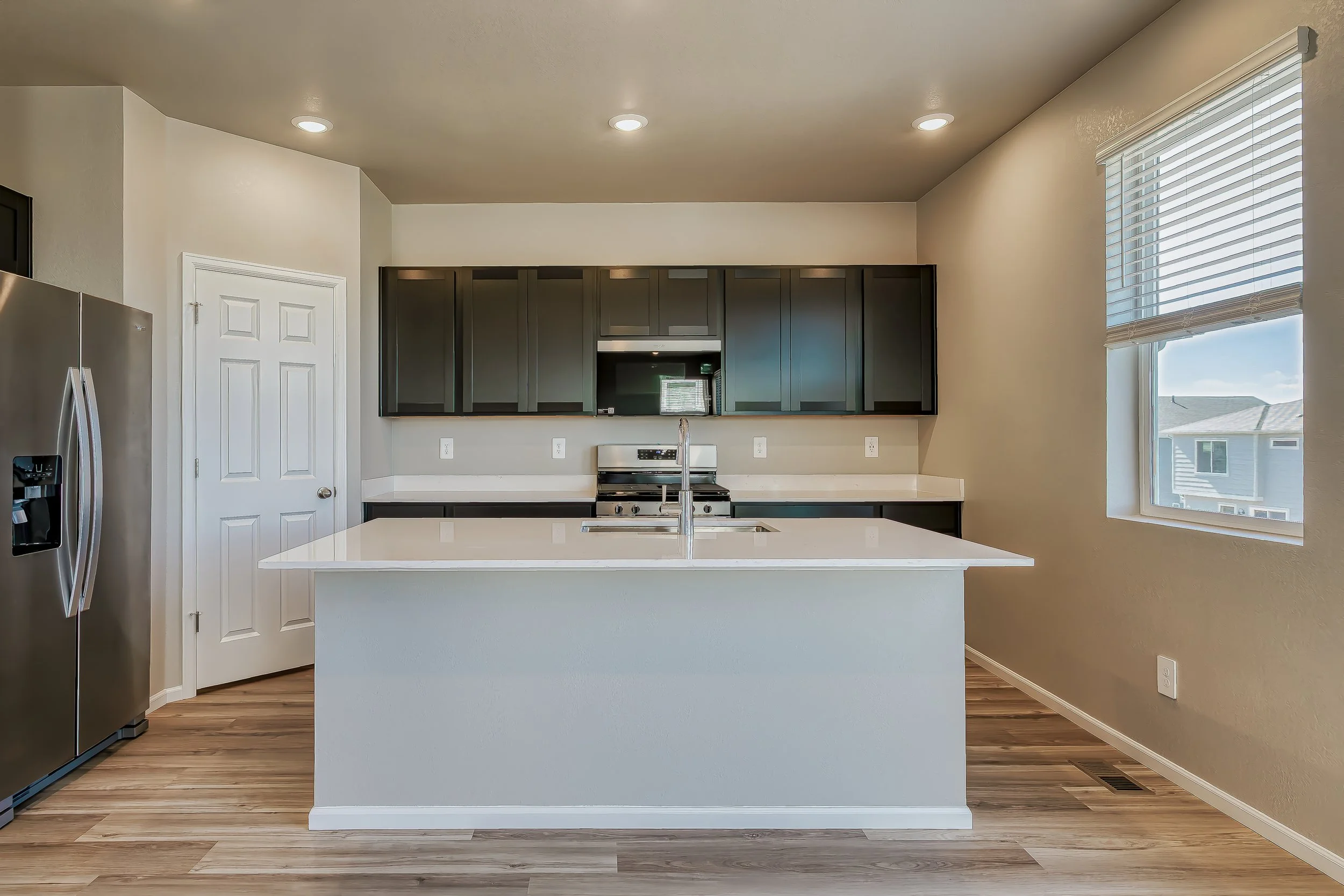 Kitchen with dark cabinets, stainless steel appliances, a white island, and a window with blinds.