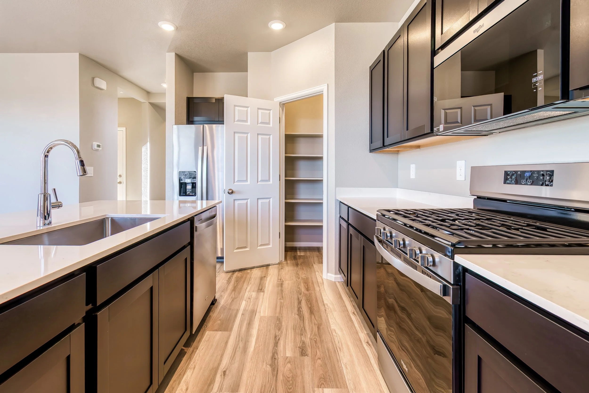 Modern kitchen with black cabinets, white countertops, stainless steel appliances, an island with a sink, and a pantry with open shelves.