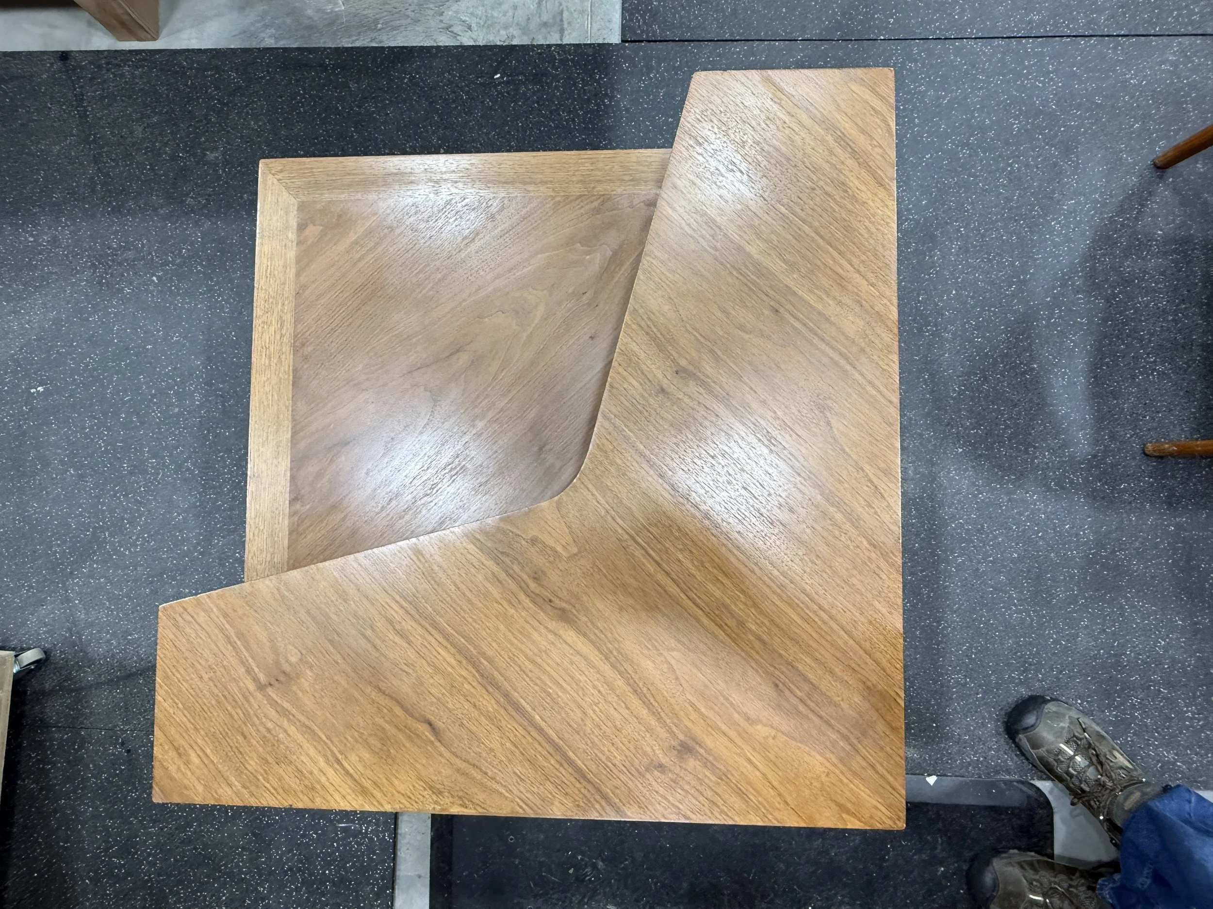 Two pieces of wooden furniture placed on a black speckled floor, with a person wearing sneakers visible at the bottom right corner.