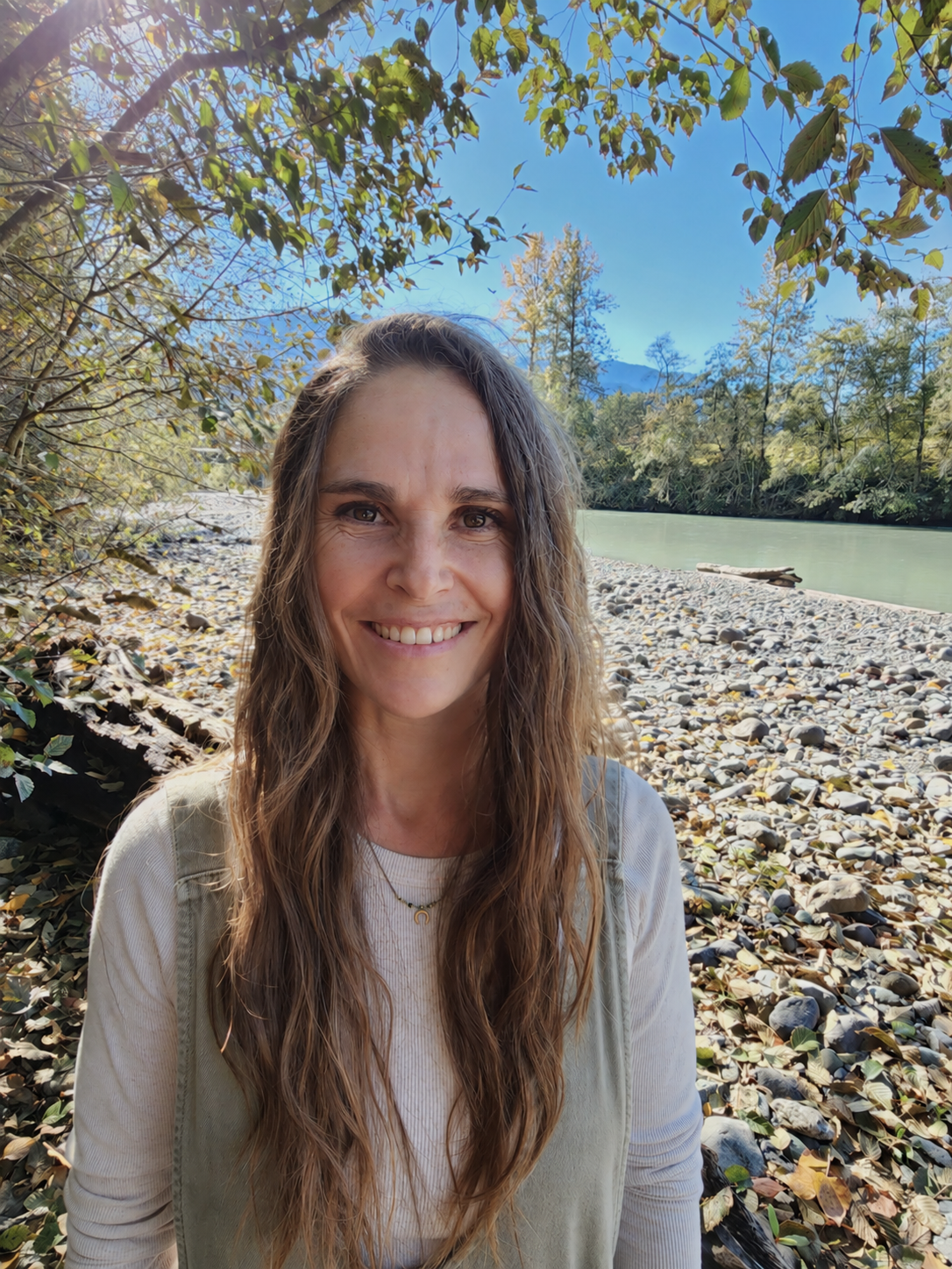 Pam DeRoo, life coach based in Squamish, BC, smiling outdoors beside a river.