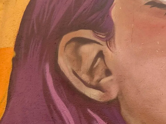 Close-up of ear and hair of a person with purple hair, painted on a textured surface.