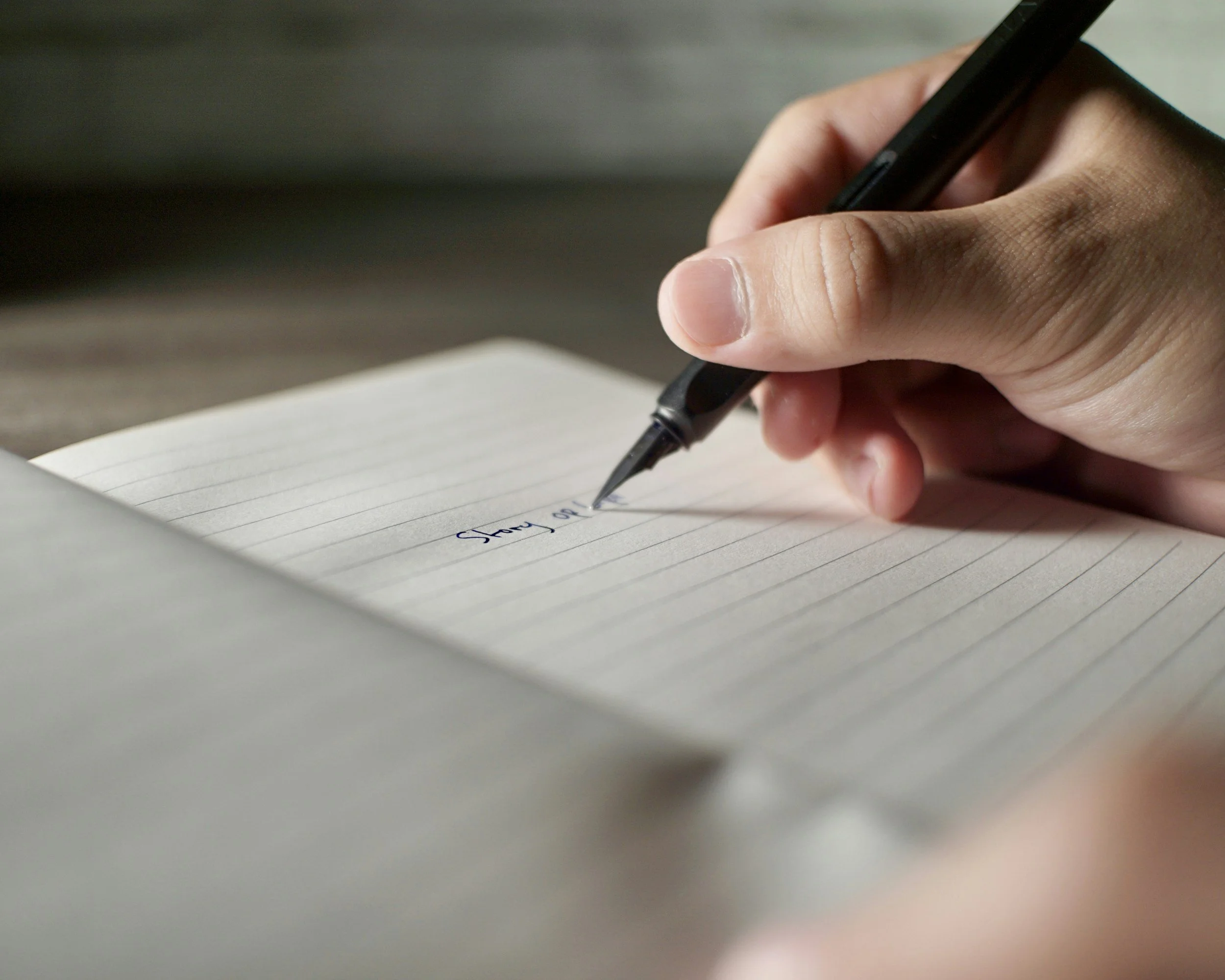 Close-up of a person's hand writing in a notebook with a black pen.