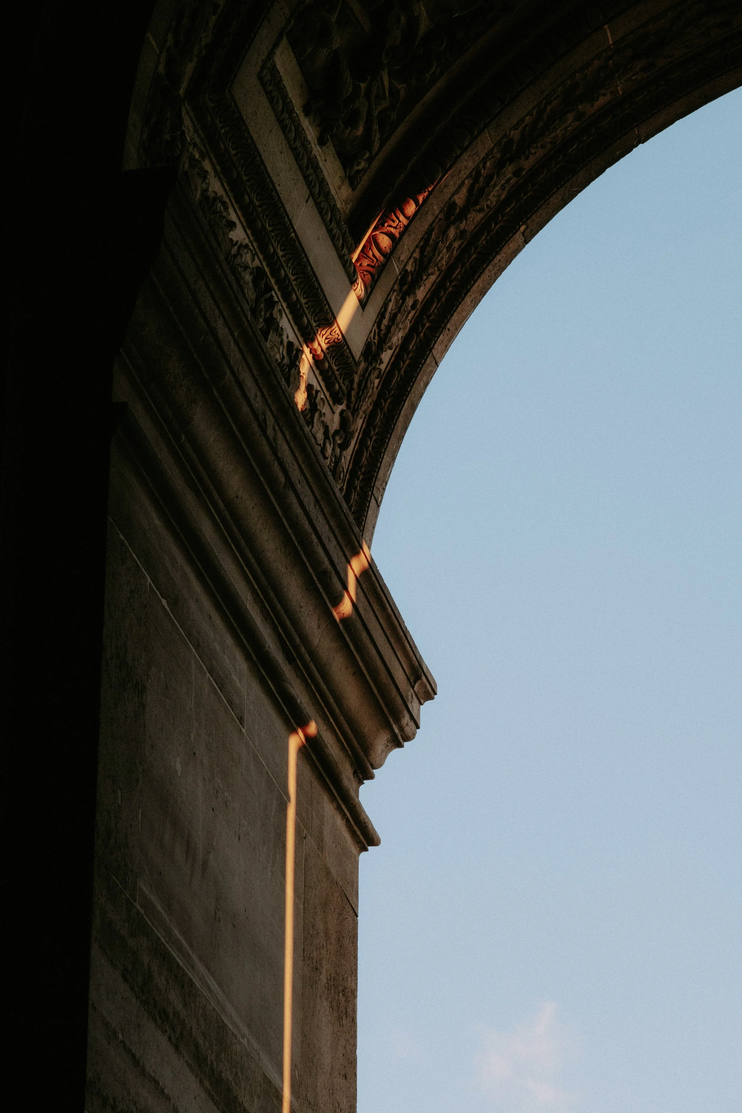 Close-up of decorative architectural details on a building's cornice, with a sunset casting a warm glow on the ornate carvings, and the sky in the background.