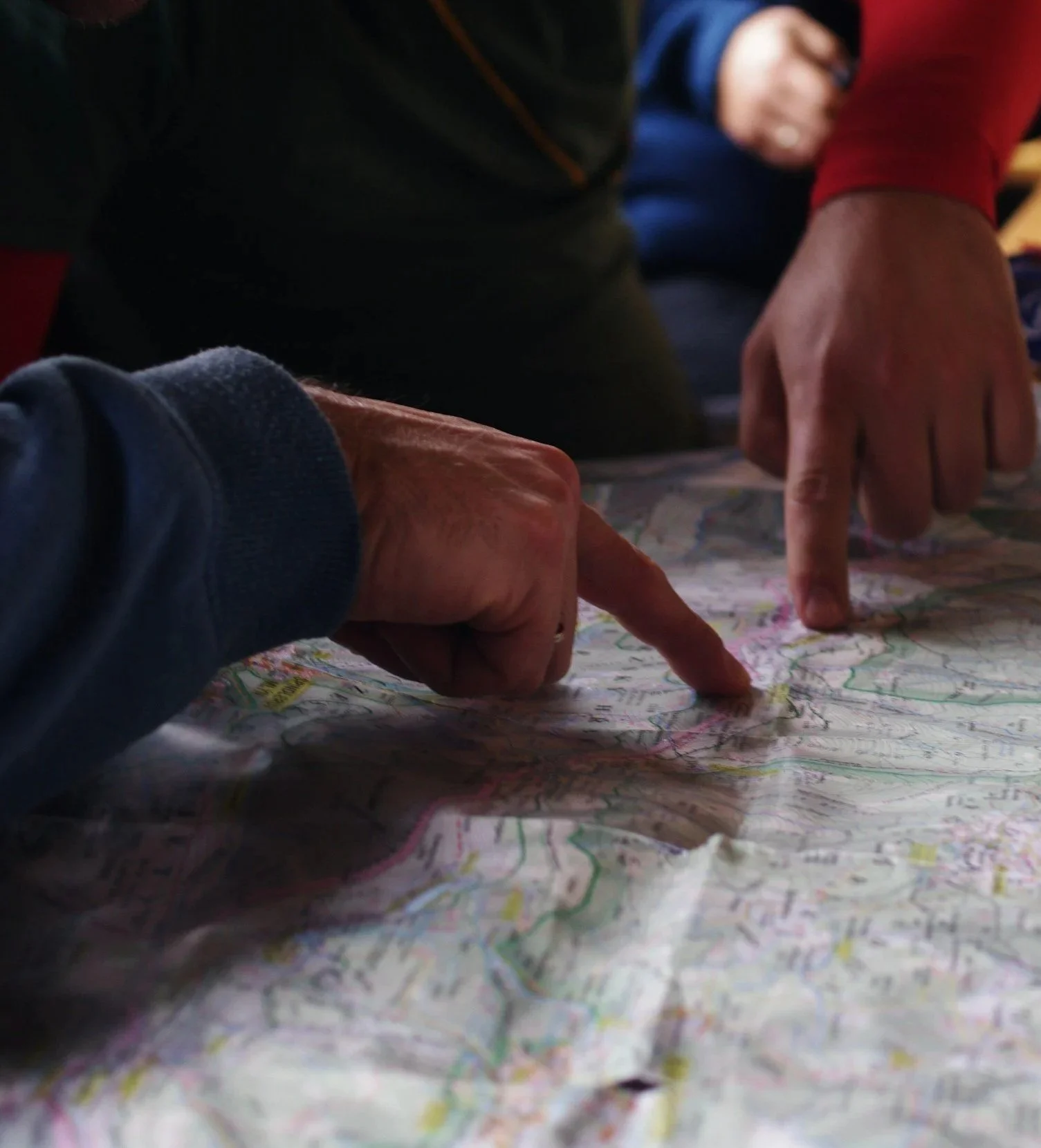 Close-up of two people using their fingers to point on a detailed paper map with various colors and markings