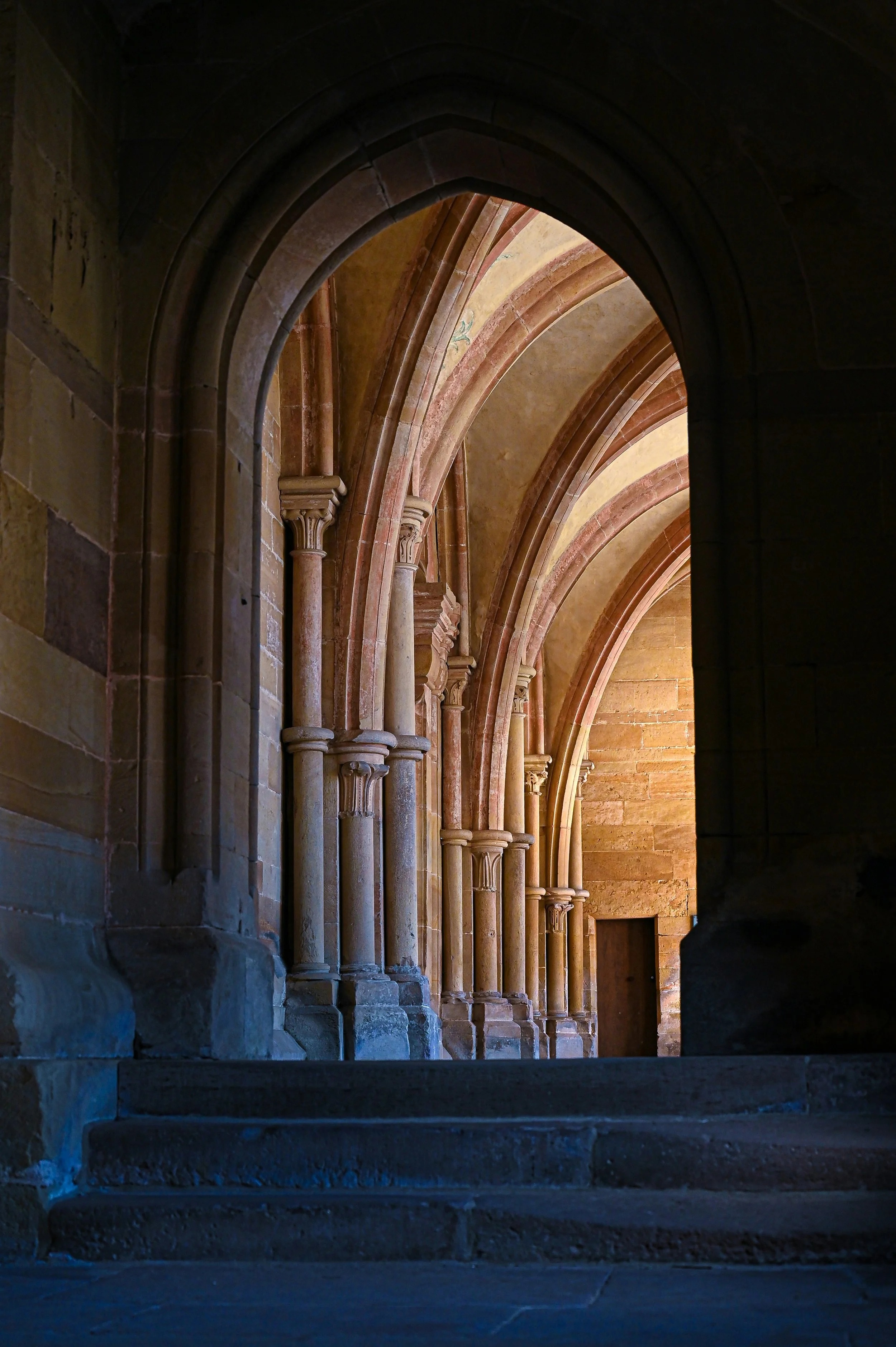 Stone archway and columns in a historic church or cathedral with tiered stairs leading up to it, lit by warm light.