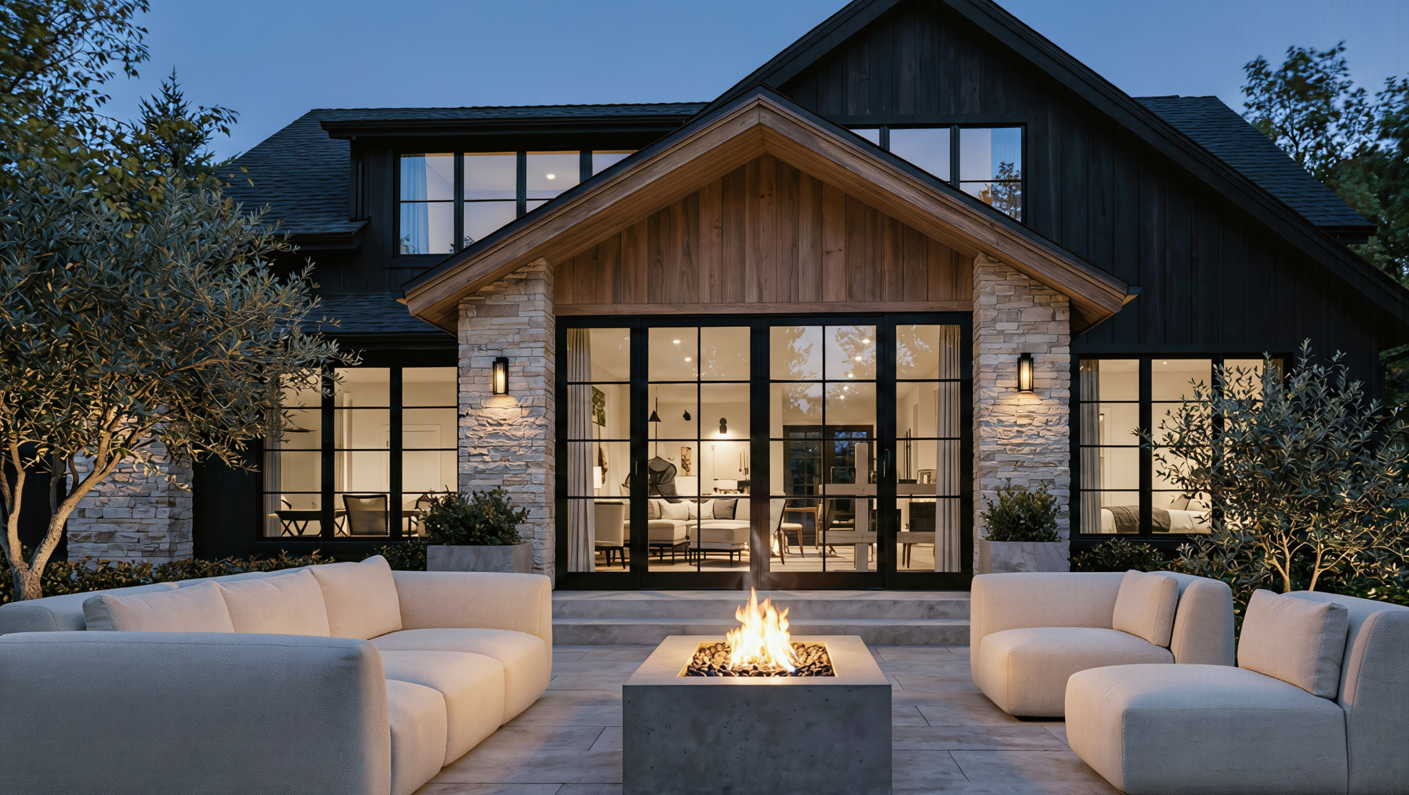 Modern house with large glass doors and windows, stone and wood exterior, outdoor patio area with couches and a fire pit.