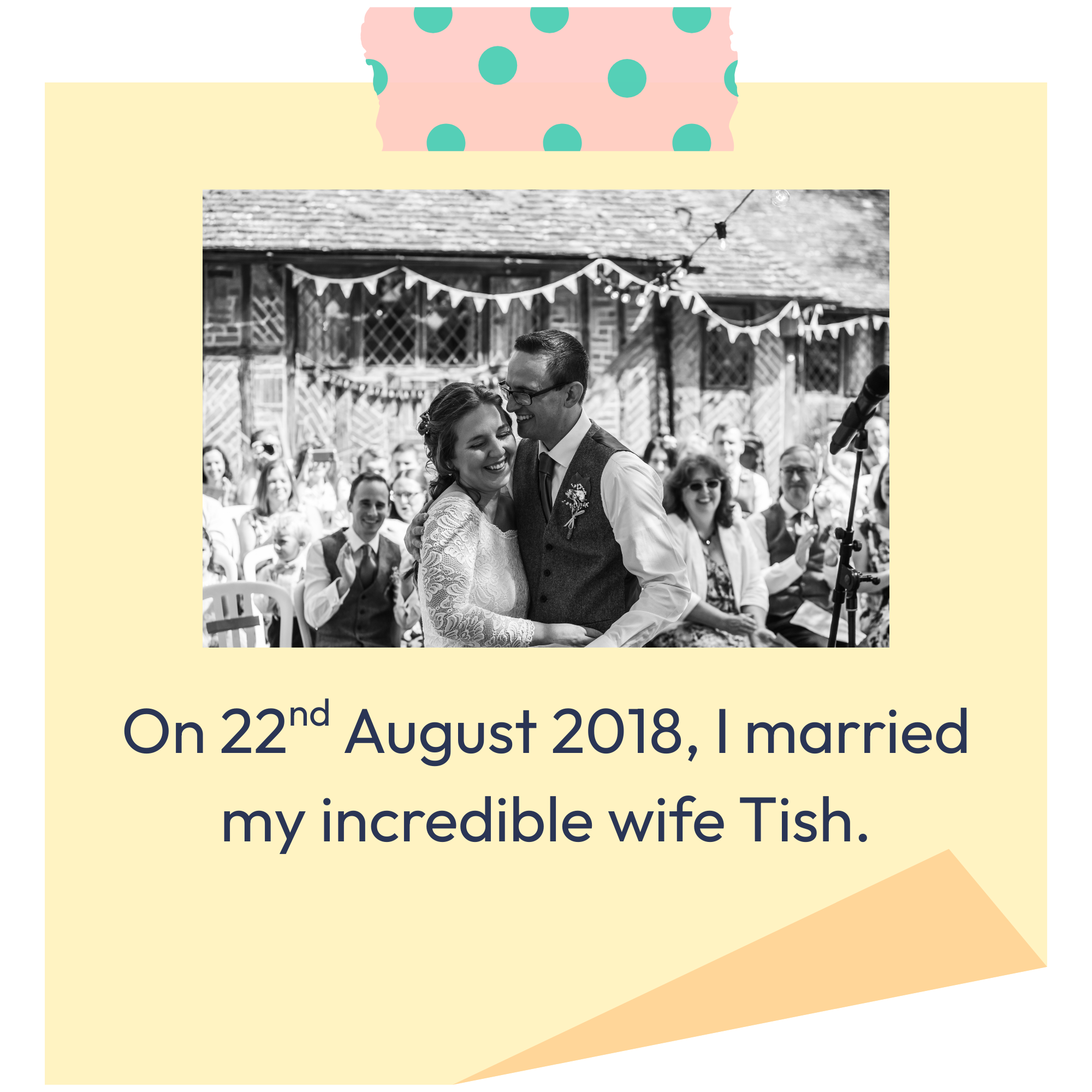 Black-and-white photo of a bride and groom embracing at their wedding, with guests in the background and bunting decorations hanging overhead.