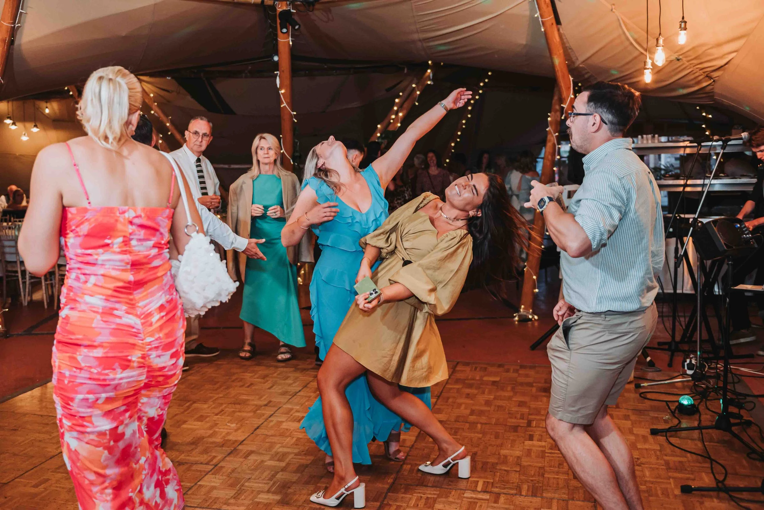 People dancing and socializing during the wedding disco at The Crescent Turner, Kent. There is warm lighting and string lights.