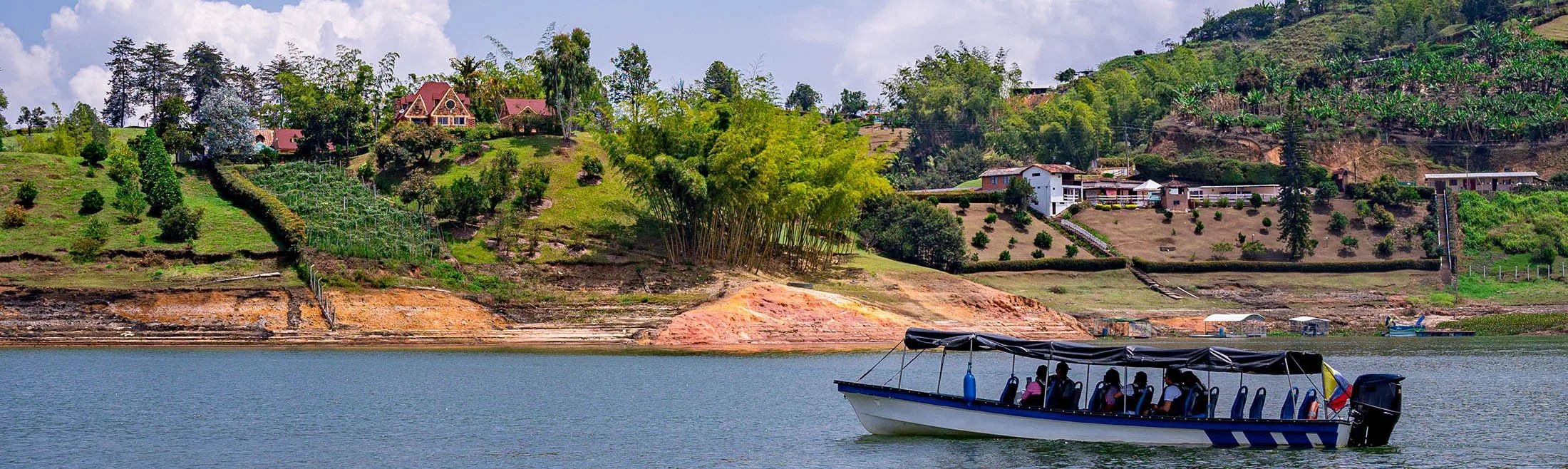 A boat with passengers on a lake, with a hilly landscape and houses in the background.