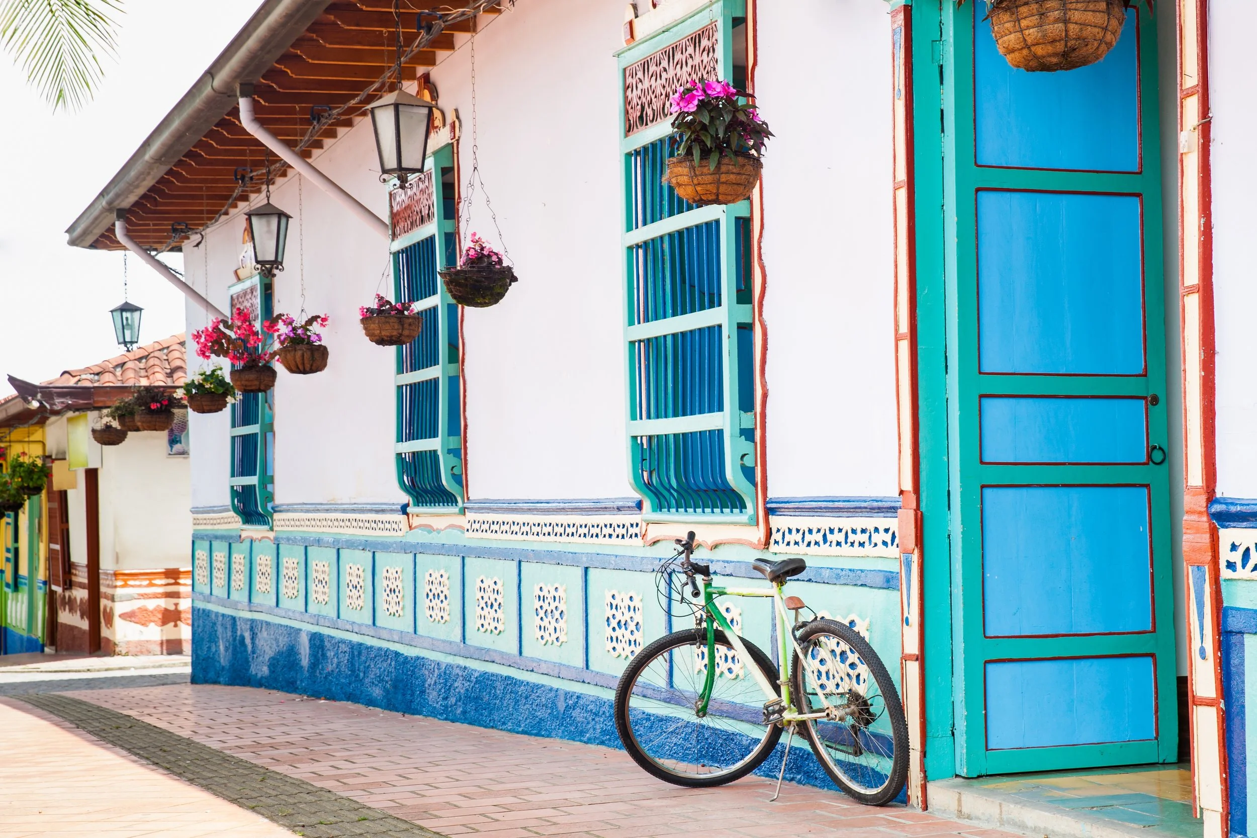 Colorful house with blue windows and door, white walls, hanging flower baskets, and a bicycle leaning against the wall.