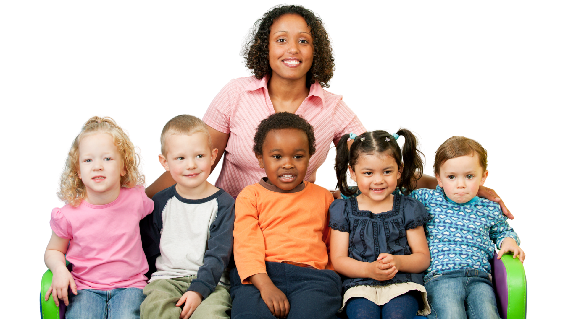 A group of six cheerful children sitting together with a woman behind them, smiling. The children include diverse ethnicities, and the woman appears to be a teacher or caregiver.
