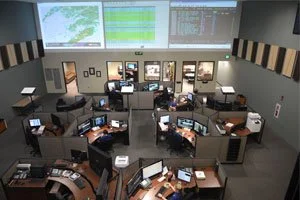 911 dispatch center control room with operator workstations and wall-mounted video displays