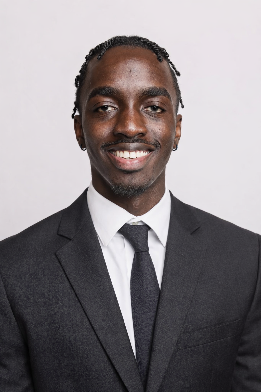 Portrait of a smiling man in a black suit, white shirt, and black tie against a plain background.