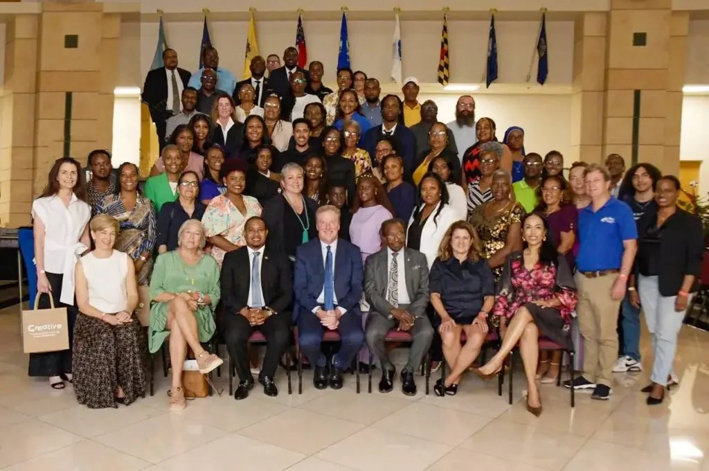Group photo of diverse people at a formal event, with flags in the background.