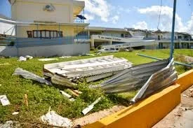 Collapsed boat or dock debris on a grassy area near houses, with broken wood and metal pieces scattered around.