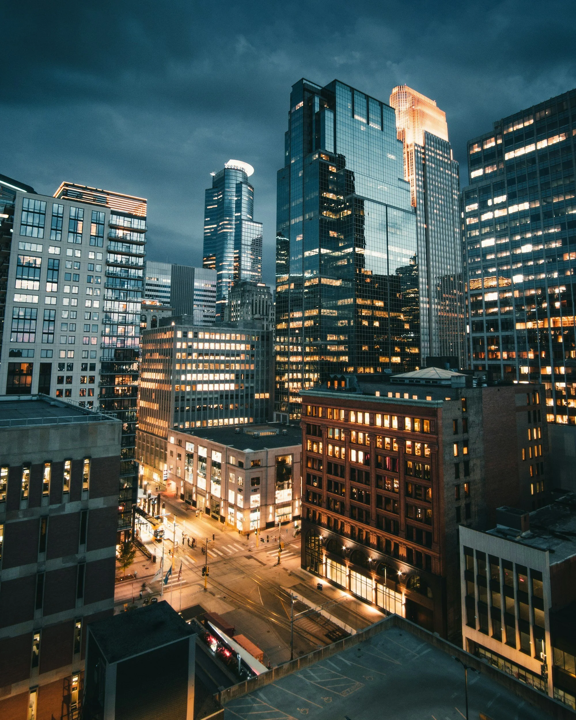 Nighttime cityscape of tall skyscrapers with illuminated windows in downtown area.
