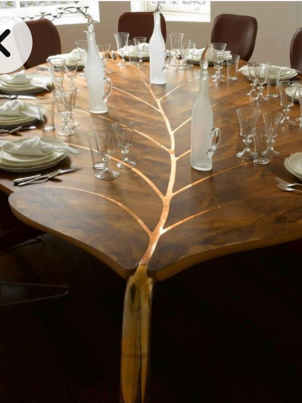 A wooden dining table with a natural, tree branch-inspired design, set for a meal with plates, folded napkins, numerous wine glasses, and decorative frosted glass bottles as centerpieces.