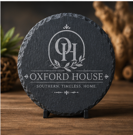 Round black slate sign with white lettering and decorative elements, reading "Oxford House, Southern. Timeless. Home."
