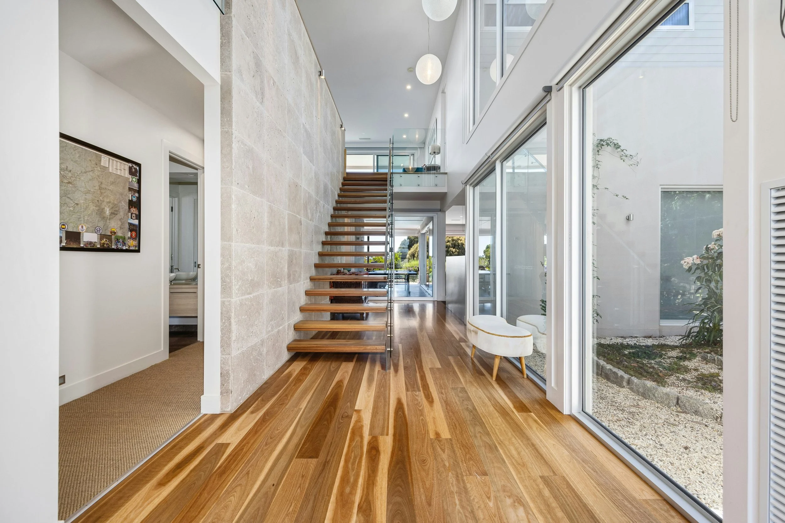 Modern interior with a staircase, wooden flooring, large glass windows, and a small stool near the window.