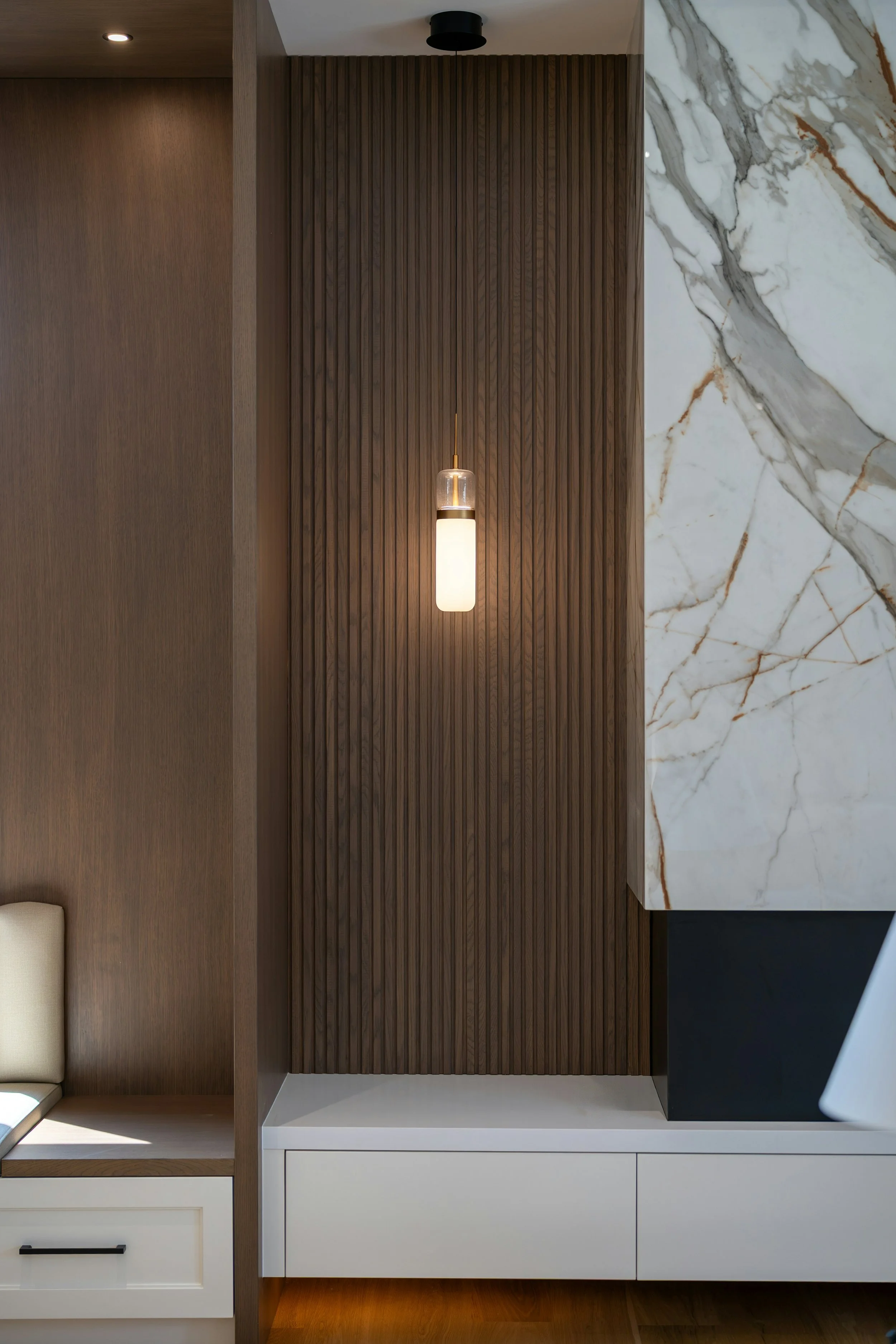 Modern interior wall with wood paneling, marble extension, and a hanging light fixture.