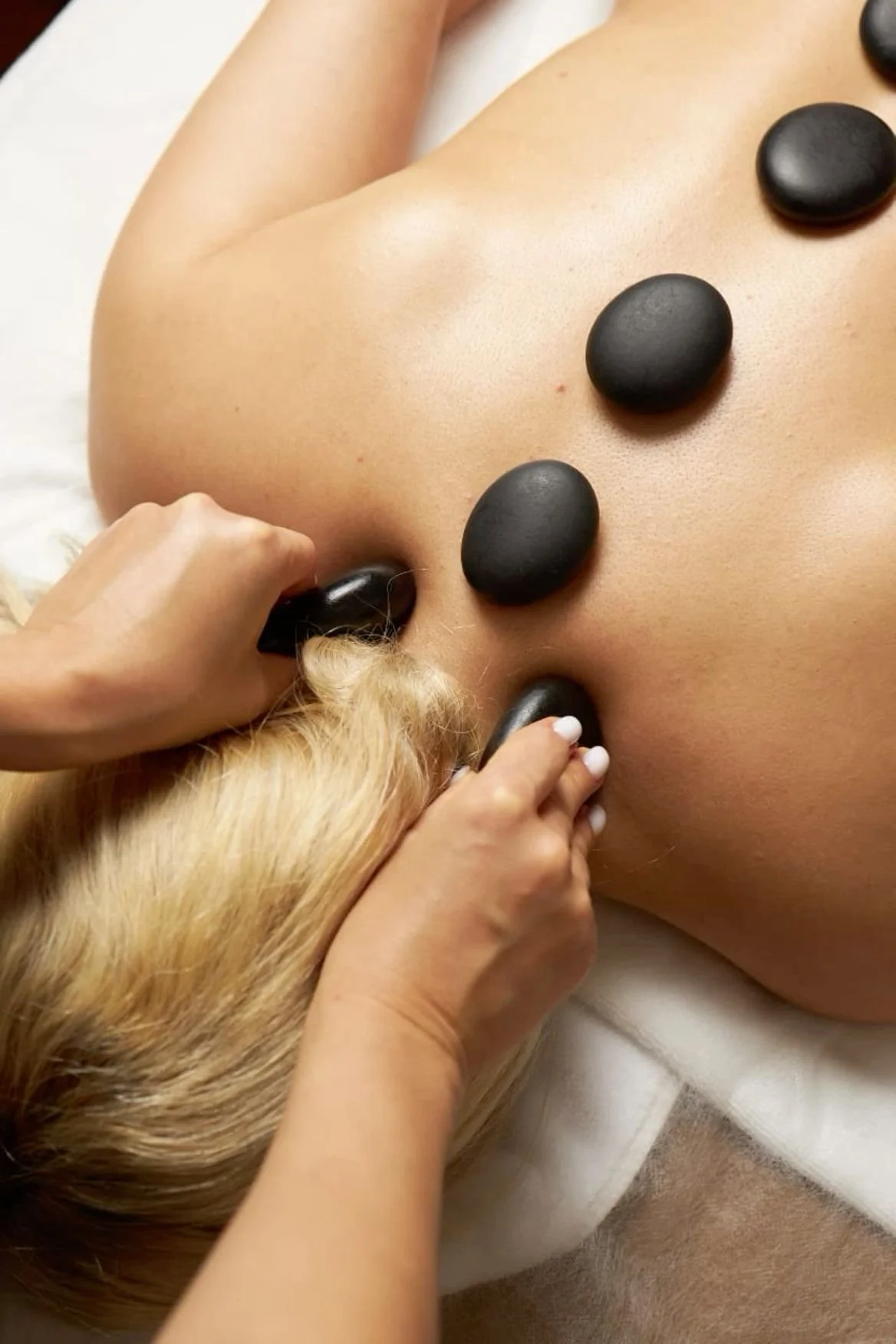 Person receiving hot stone massage with black stones placed on their back.