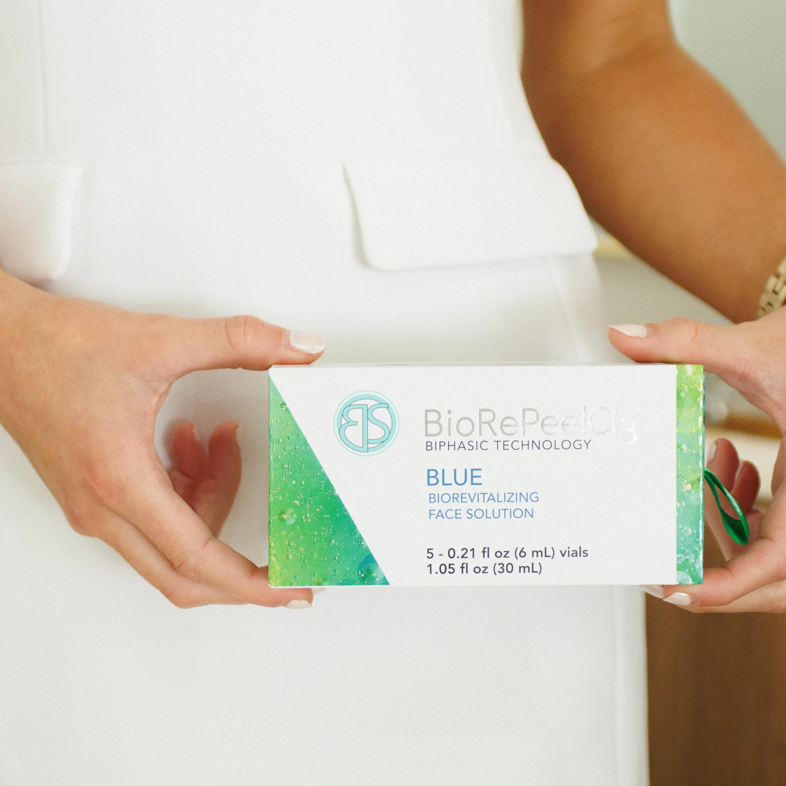 Hands holding a box of BioRePeel33 Blue Biorevitalizing Face Solution in front of a white background.