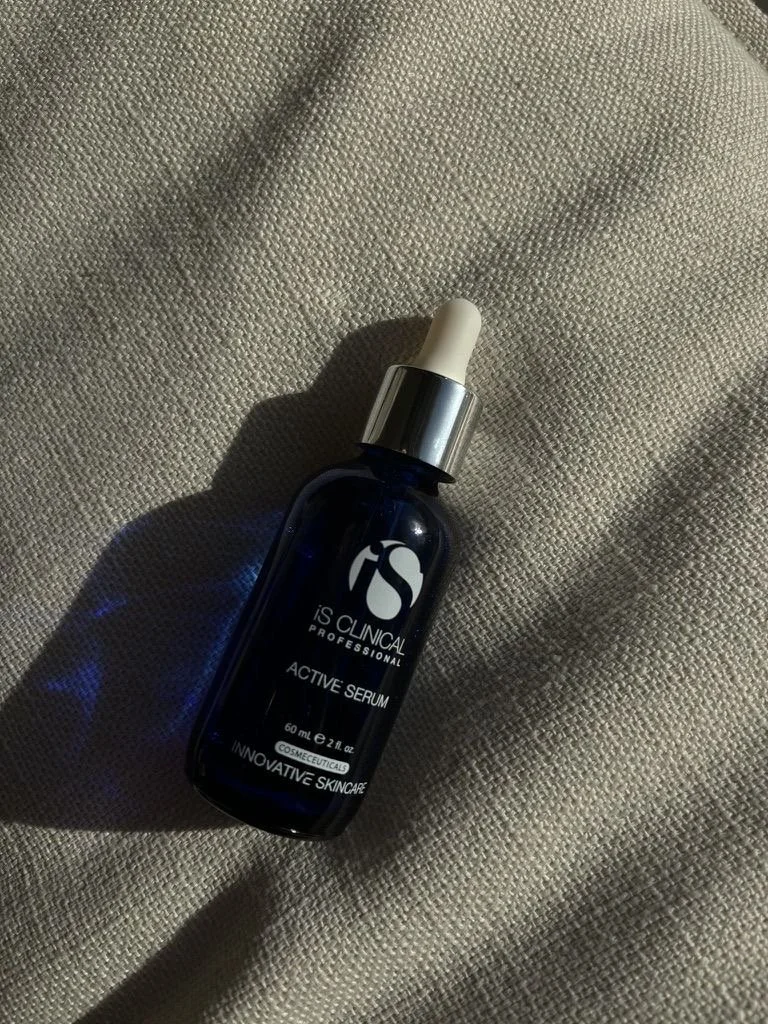A dark blue bottle of IS Clinical Active Serum with a white dropper cap resting on a textured beige fabric surface.