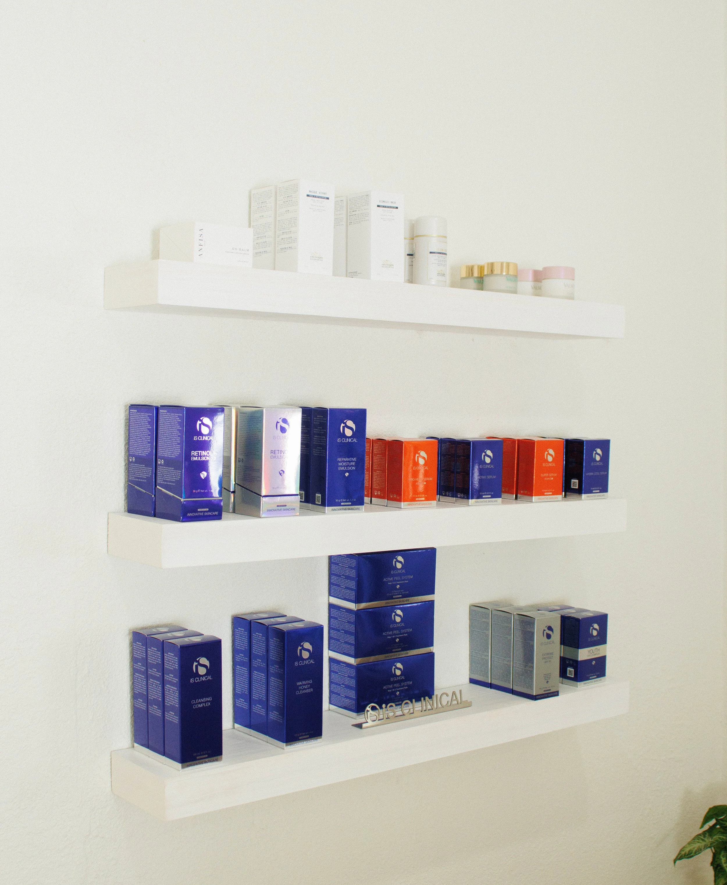 White wall-mounted shelves displaying skincare products such as iS Clinical, Valmont, Anfisa, Biologique Recherge and Forlled