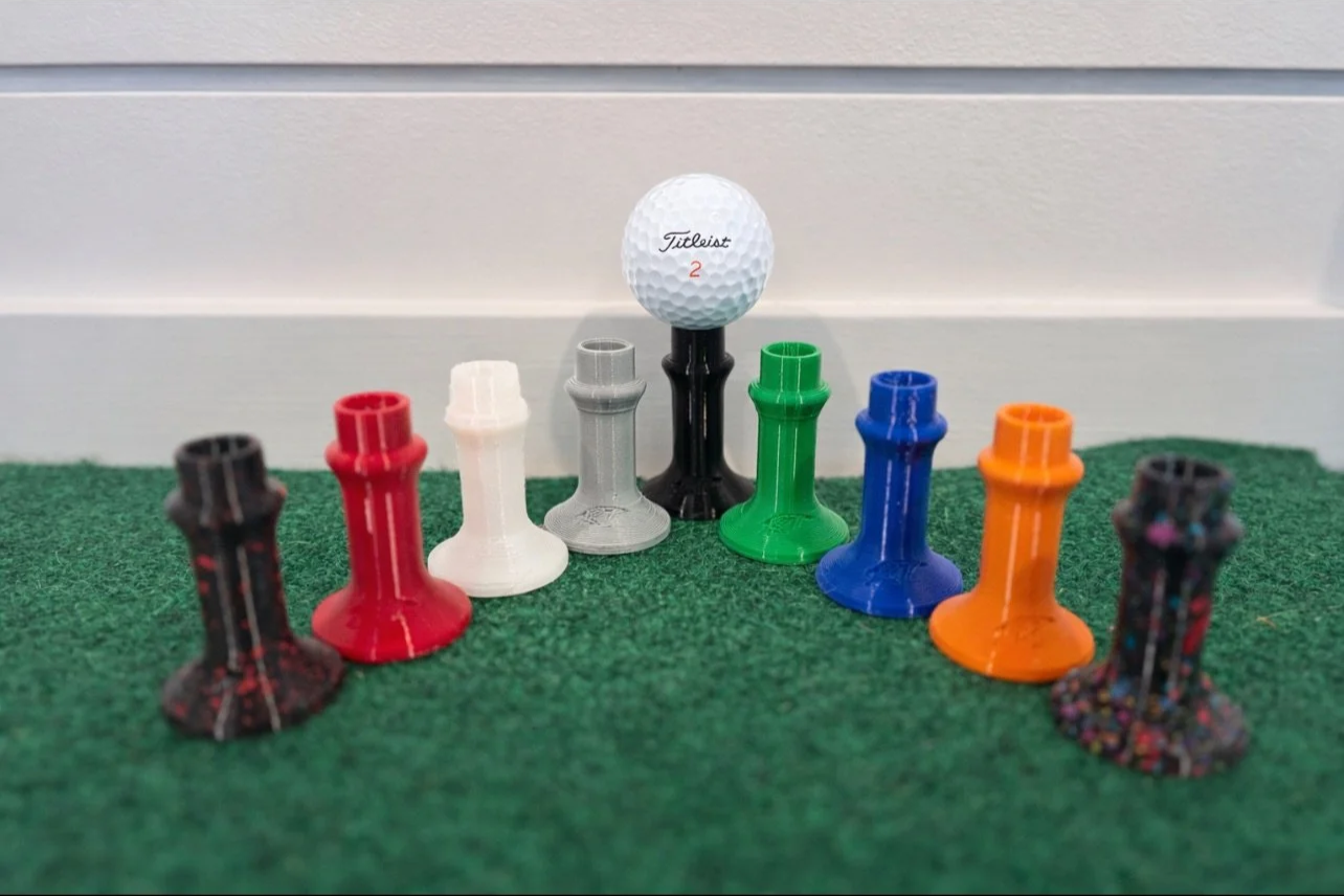 Colorful golf tees arranged on green turf with a golf ball on a tee in the center.