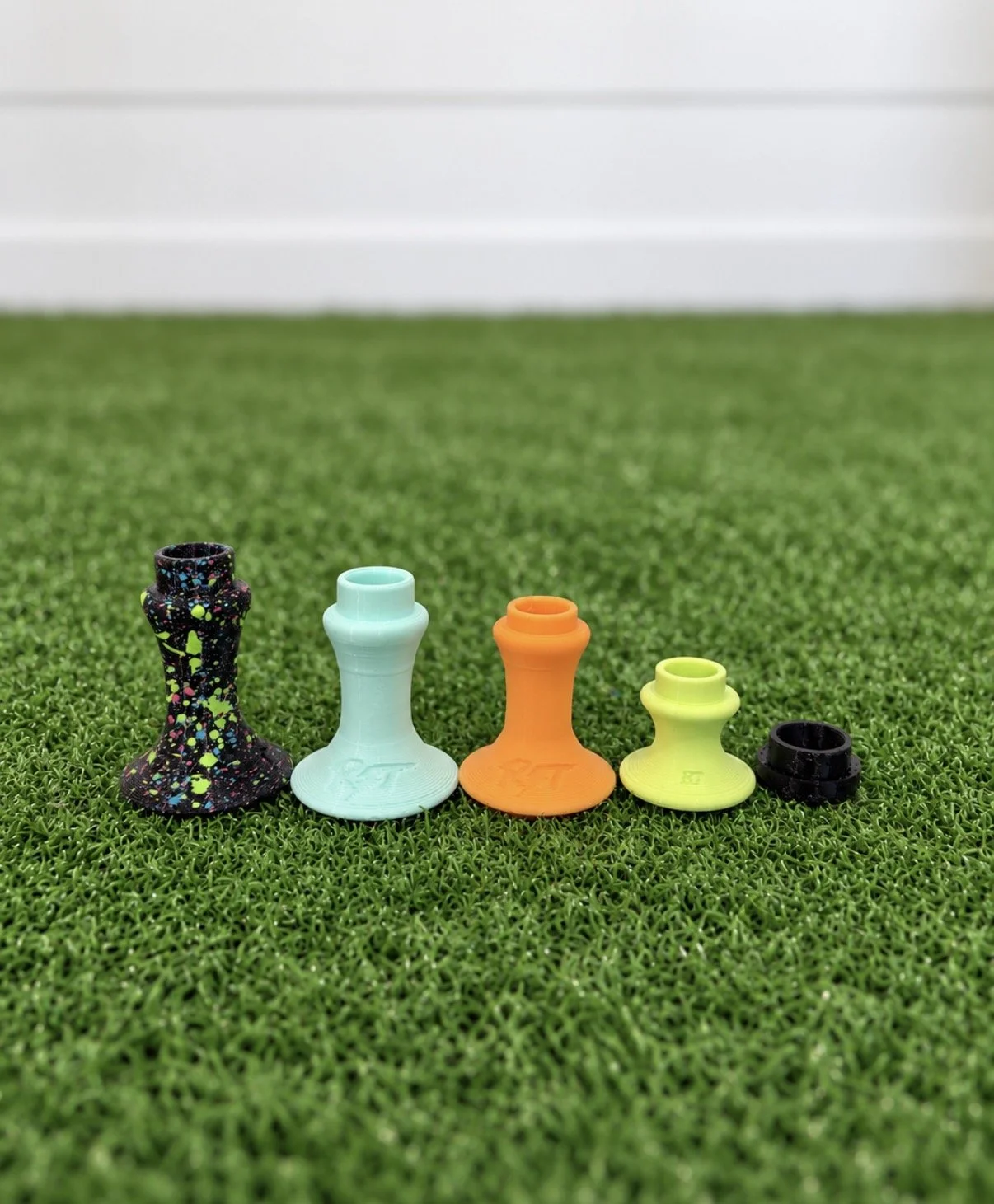 Colorful chess pawns arranged on green turf with a white wall in the background.