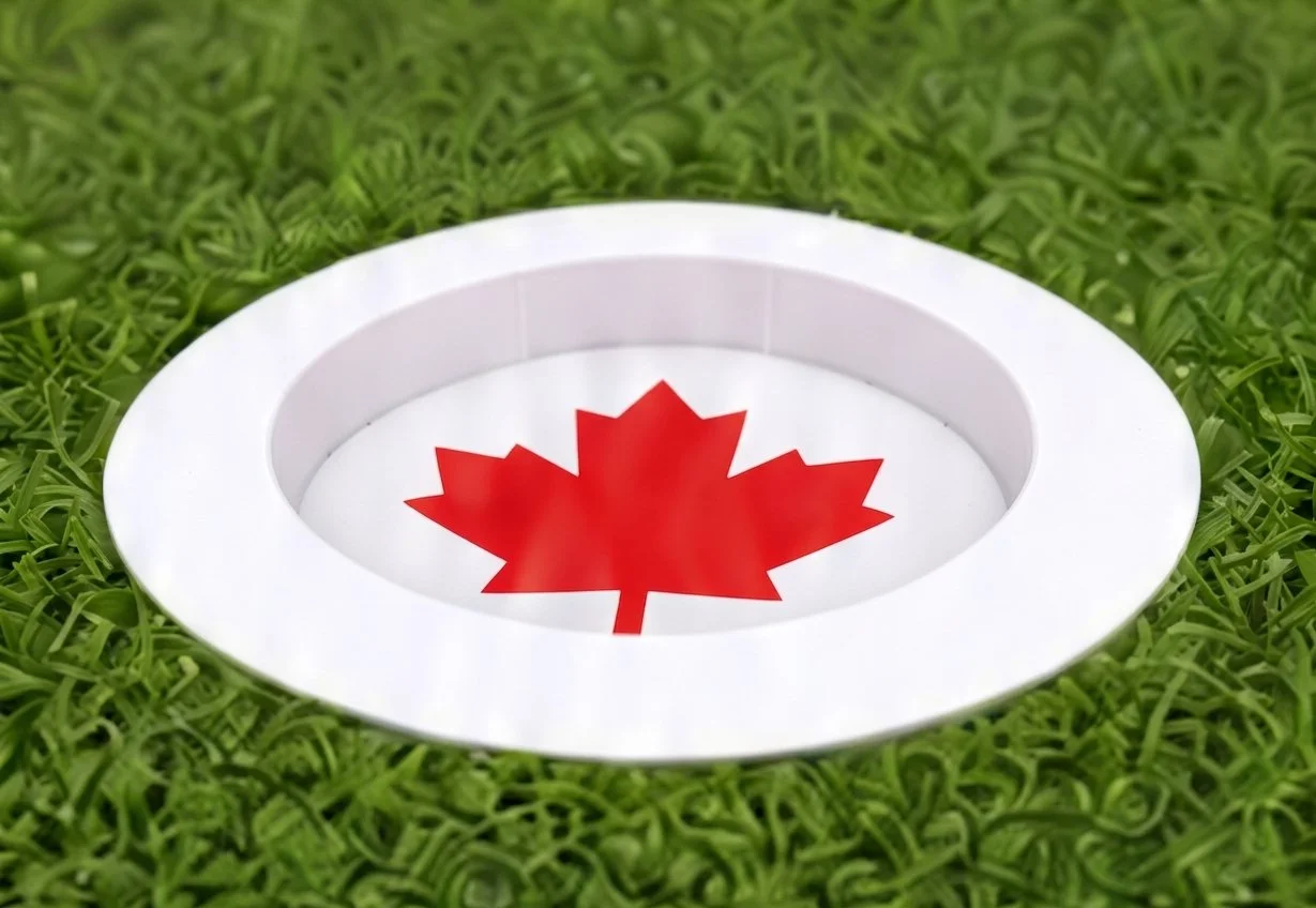 A white circular opening in the grass revealing a red maple leaf symbol, representing Canada.