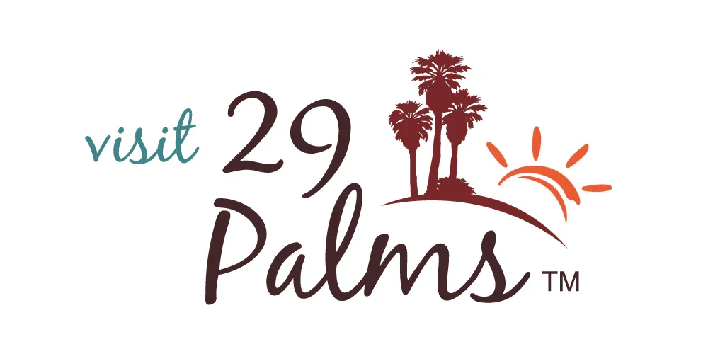 Logo with the words "visit 29 Palms" featuring a silhouette of three palm trees, a sun with rays, and a curved line representing the horizon.