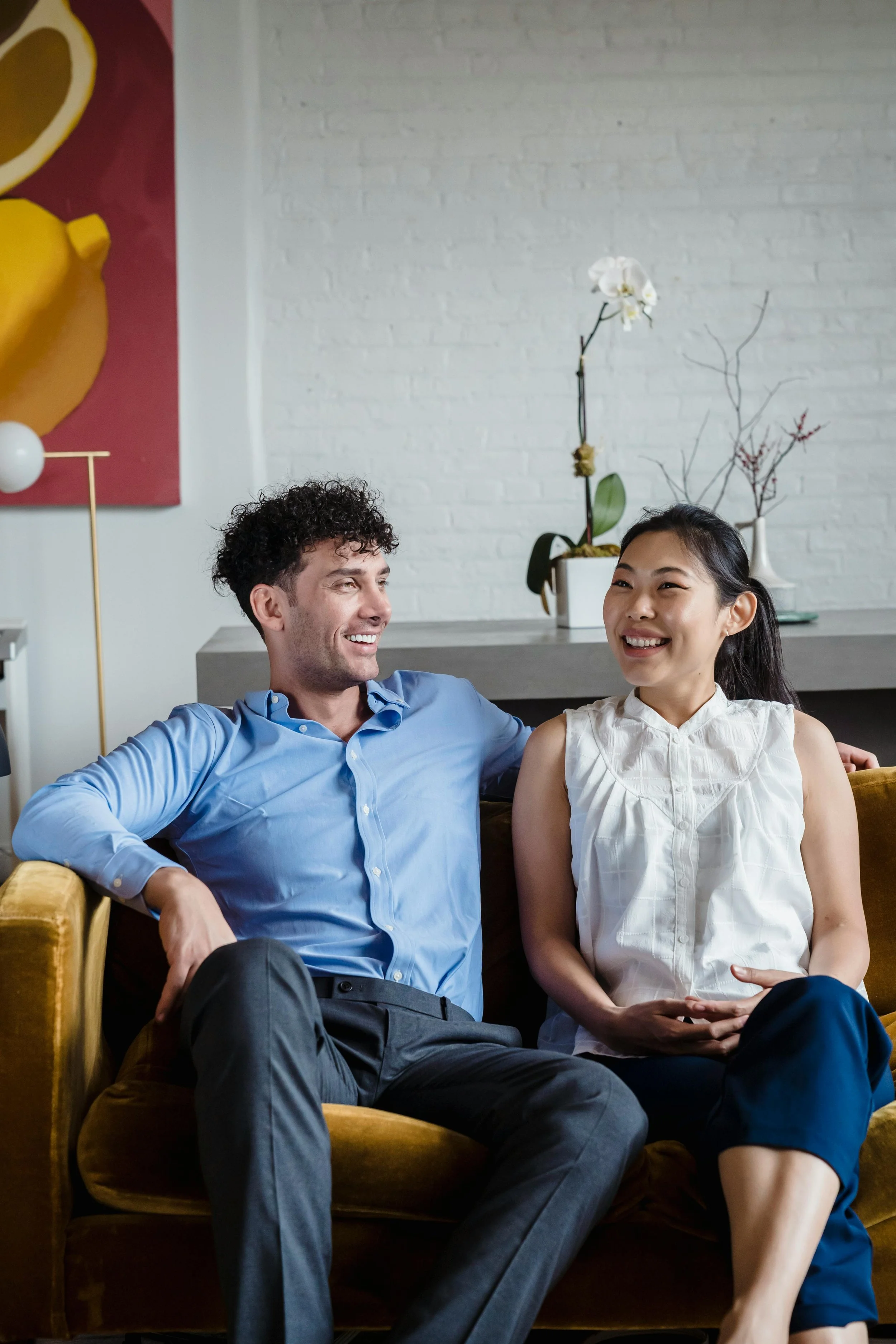Couple smiling and connected on a bright couch, representing the relational ease that can follow EMDR intensive work at Healthy Mind, Healthy Heart