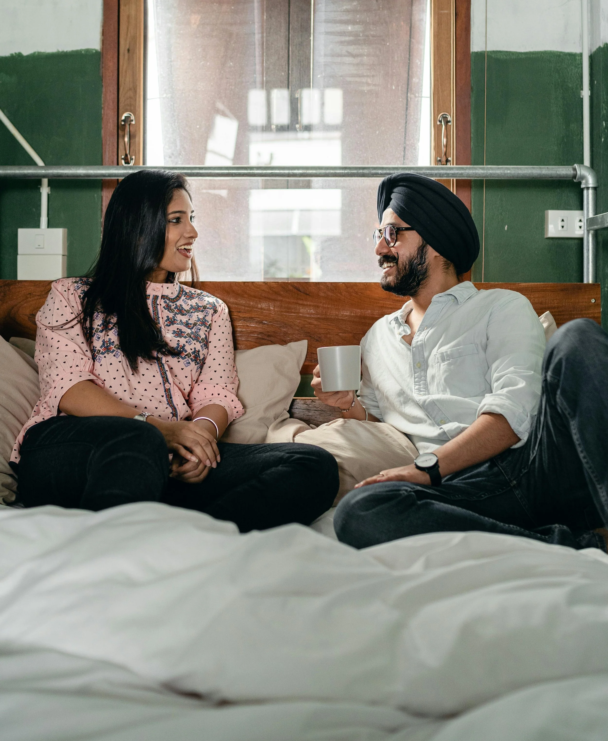 Couple smiling and connected on a bed in soft daylight, representing the relational ease that follows couples therapy when the work actually reaches what's underneath