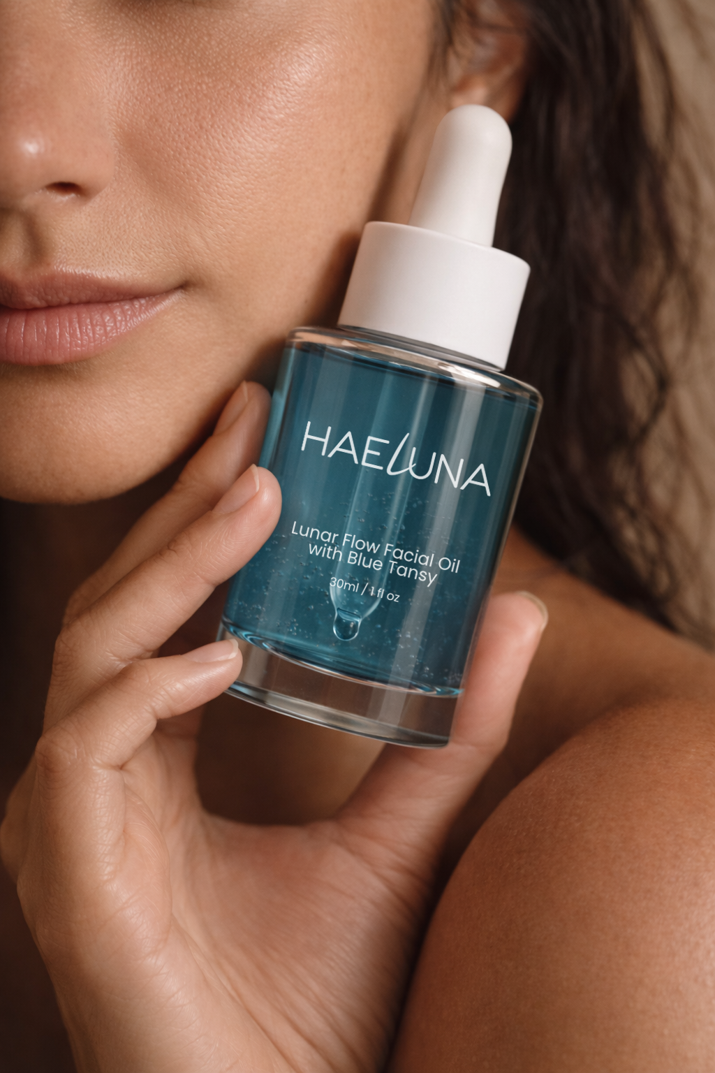 A person holds a bottle of HAELUNA Lunar Flow Facial Oil with Blue Tansy close to their face.