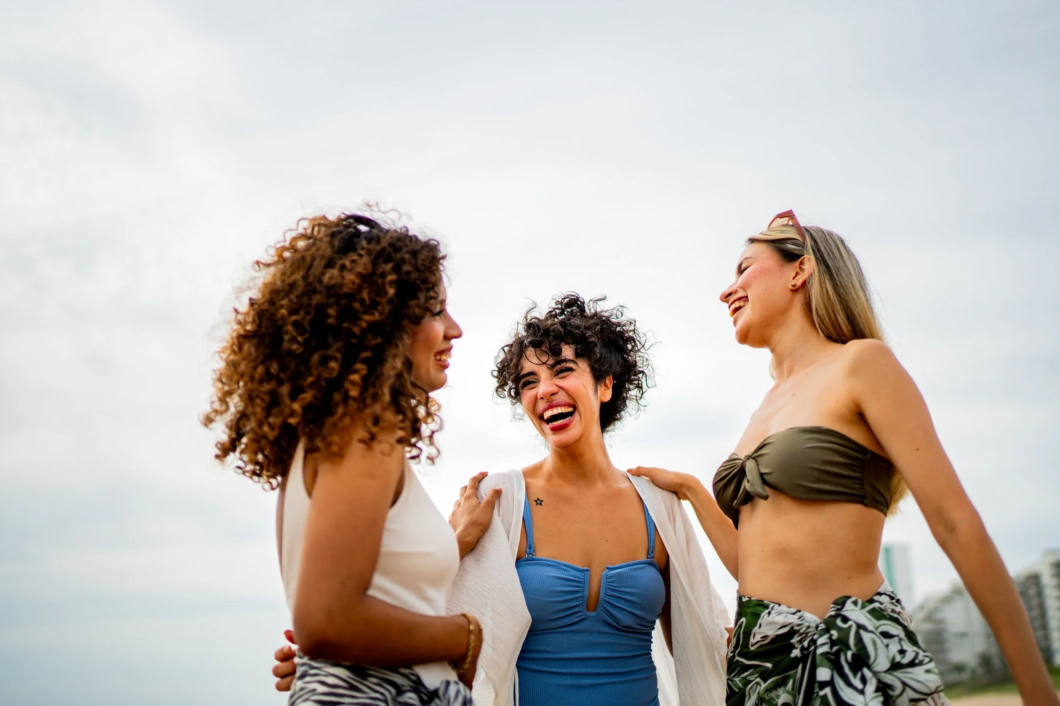 3 Women on a beach in bikinis and great skin laughing all hugging