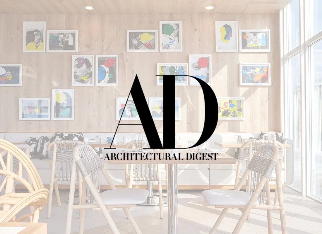 Bright, modern dining area with wooden walls, colorful abstract art on the wall, rattan chairs with cushions, a round glass table, and large windows allowing natural light.