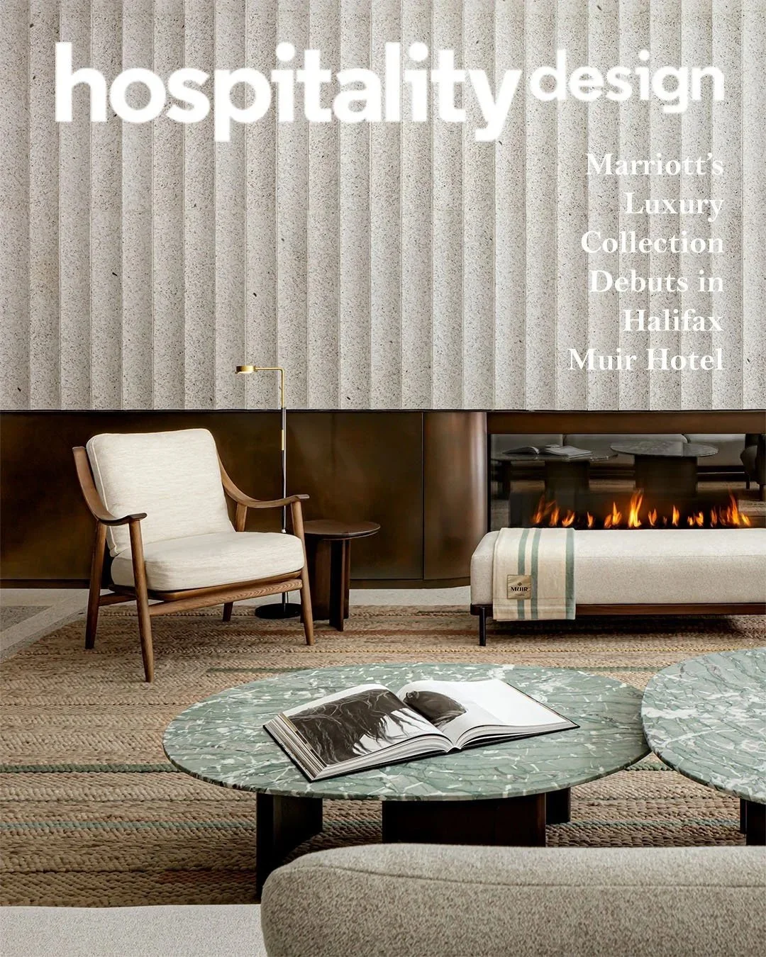 Interior of a hotel lobby featuring a cream armchair, a small wooden side table, a modern fireplace, and a marble-top coffee table with an open book, with text overlay about hospitality design and Marriott's luxury collection debut in Halifax at the 
