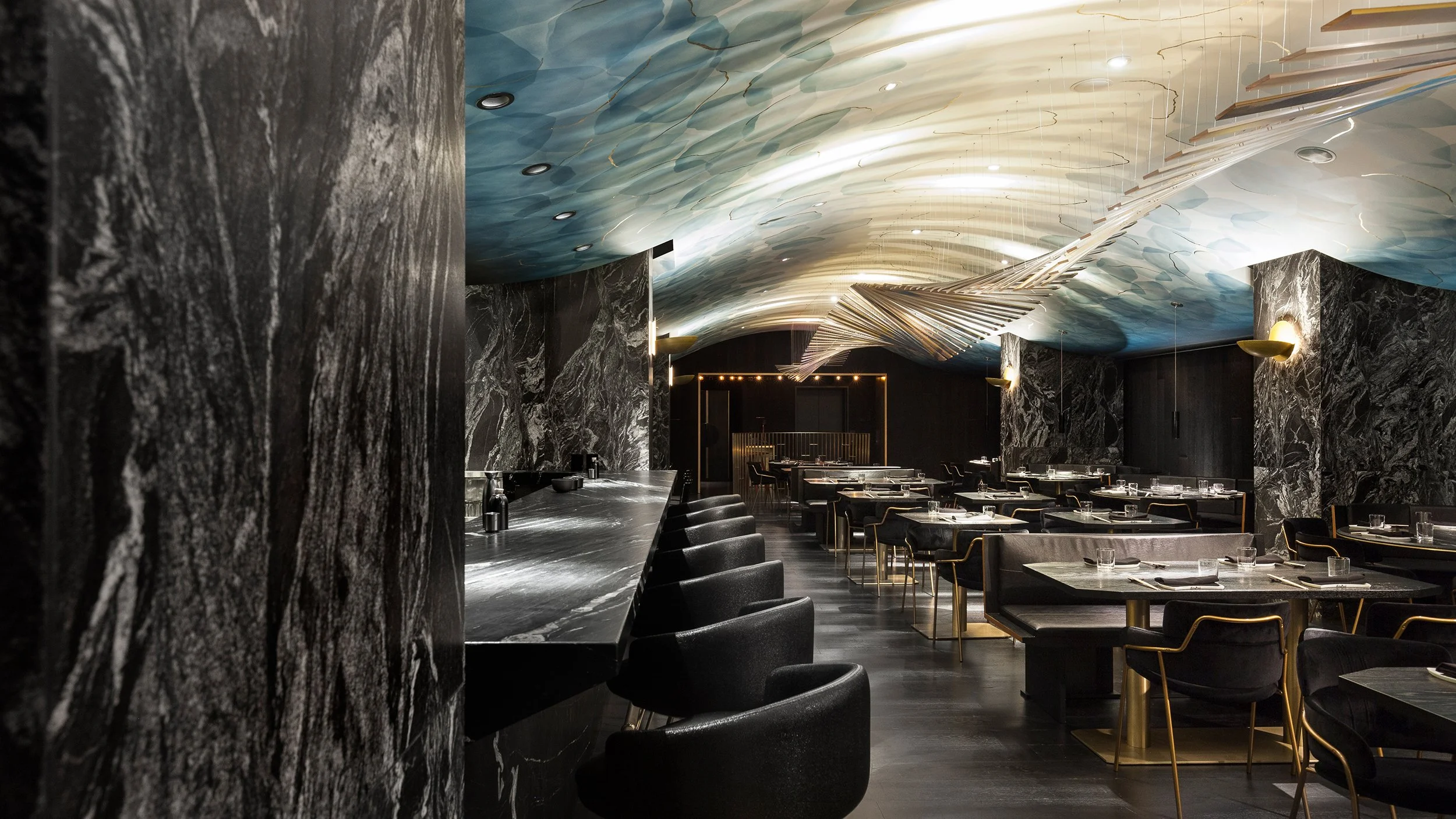 Elegant restaurant interior with dark marble walls, a sweeping artistic ceiling design, and modern black tables and chairs.