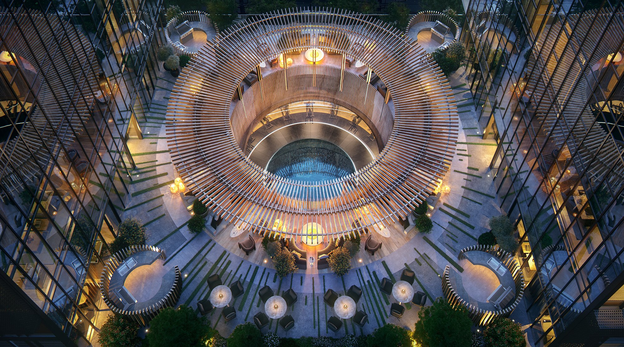 Aerial view of a modern indoor courtyard with a circular water feature at the center, surrounded by curved wooden slats forming a spiral pattern. There are lounge chairs, small tables, and potted plants around the courtyard, with seating areas and warm lighting.