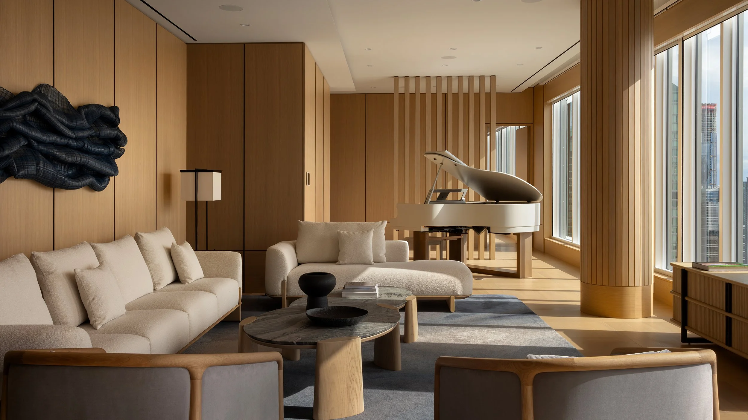 Modern living room with large windows, white couch, black coffee table, and a white grand piano.