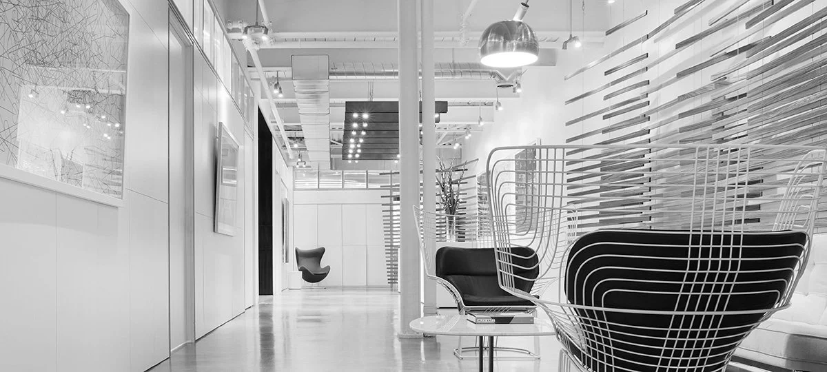 Modern interior office space with white walls, contemporary chairs, artwork on the wall, and a sleek ceiling design.
