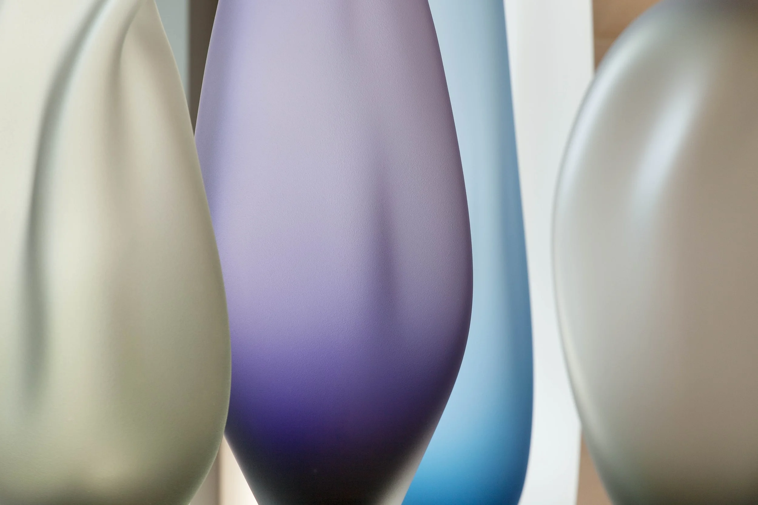 Close-up of pastel-colored vases in shades of cream, purple, blue, and green.