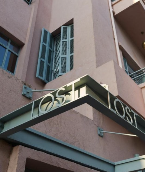 Photo of a building with pastel pink walls, blue window shutters, and a sign that reads 'LOST' mounted on an overhang.