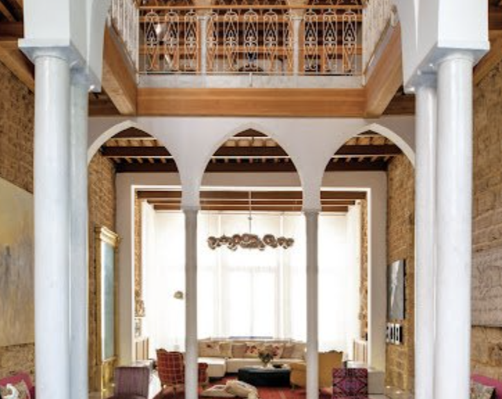 Living room with high ceiling, large window, white curtains, beige and pink furniture, decorative chandelier, and archways.
