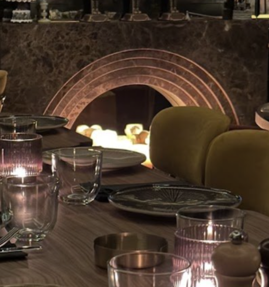 A dining table set with plates, glasses, and candles in front of a fireplace.
