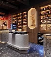 Modern bar with a gray curved counter, illuminated shelves behind displaying various bottles, and a decorative sculpture in a niche
