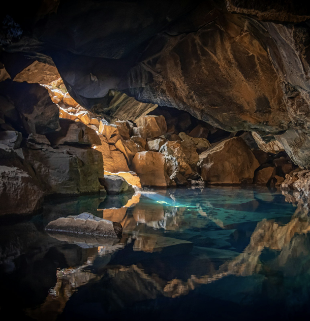 Inside a rocky cave with a clear blue water pool, illuminated by sunlight filtering through the opening.