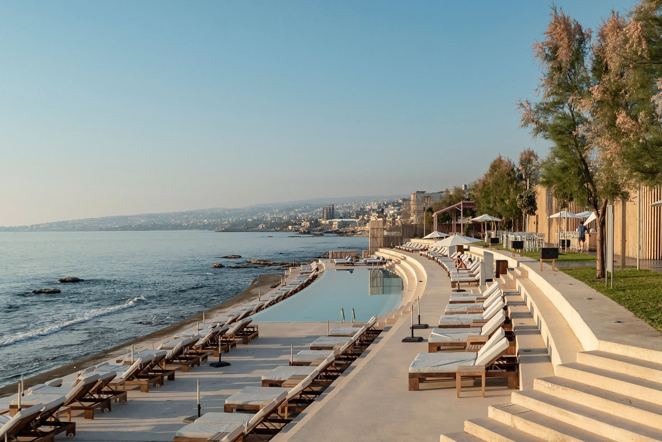 Empty poolside with lounge chairs and umbrellas overlooking the ocean during daytime.
